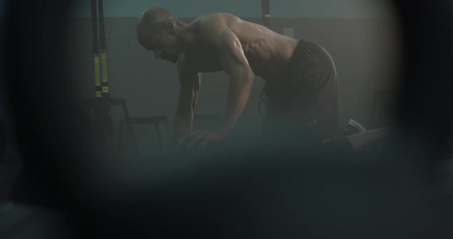 A muscular man gets on the floor and prepares to do push ups off of a small ball