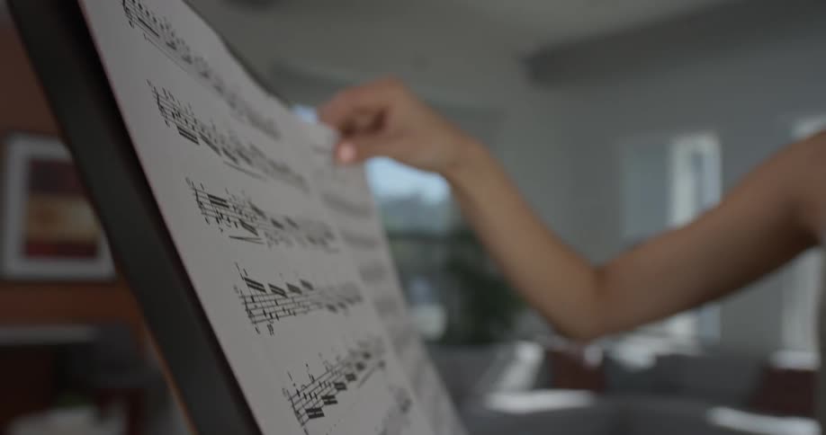A woman puts sheet music on a music stand as she holds a violin