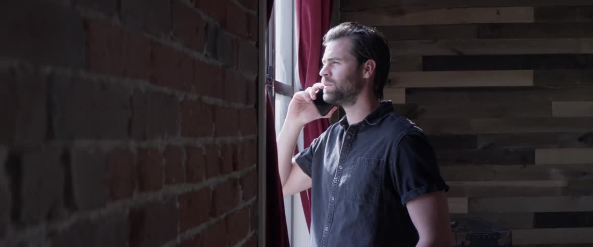 A man is talking on the phone standing by a window