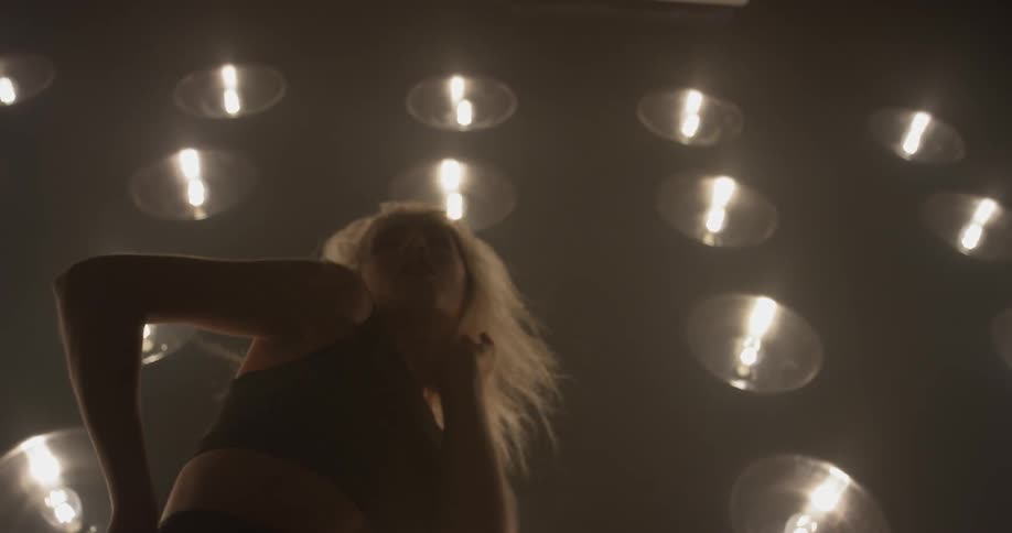 A woman does a dance routine in front of a wall of lights