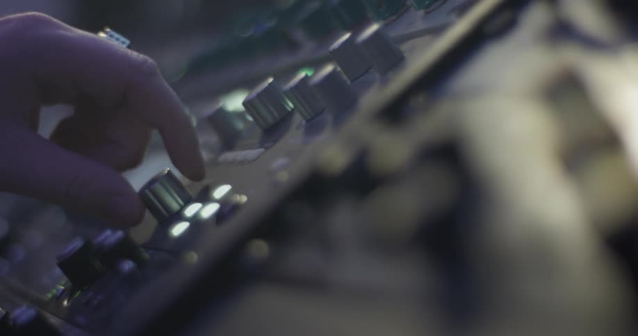 A person adjusting knobs on a mixing board