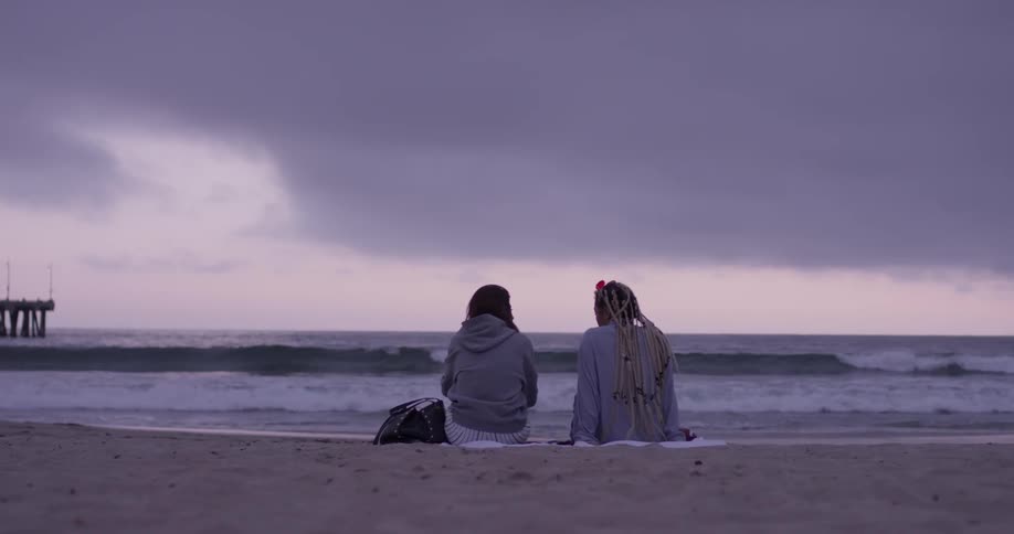 Two woman sitting in the sand looking to the water