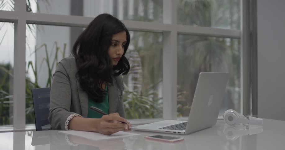 A woman reading her laptop and writing something down