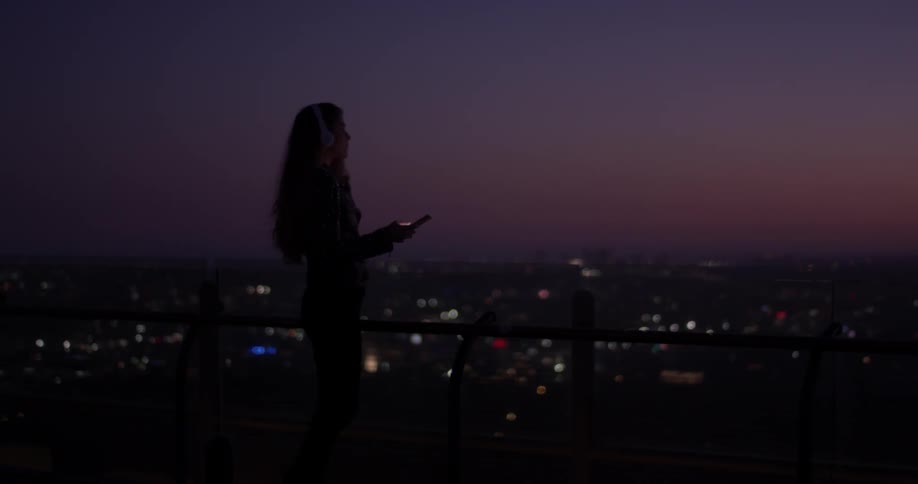 Woman looks at a phone at night with a city below