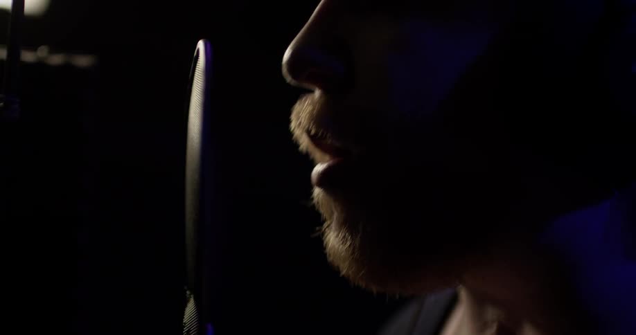 A man singing in to a microphone with a flat screen in front of it