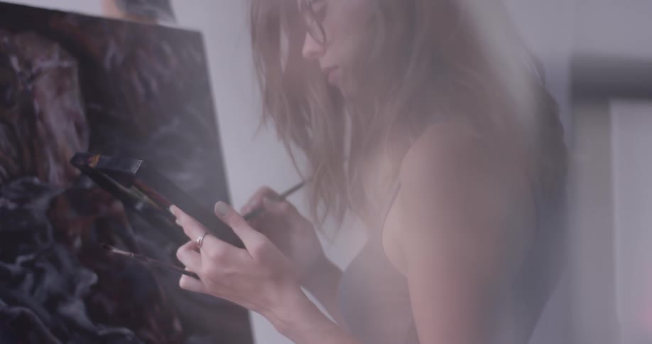 Woman paints on canvas while holding easel