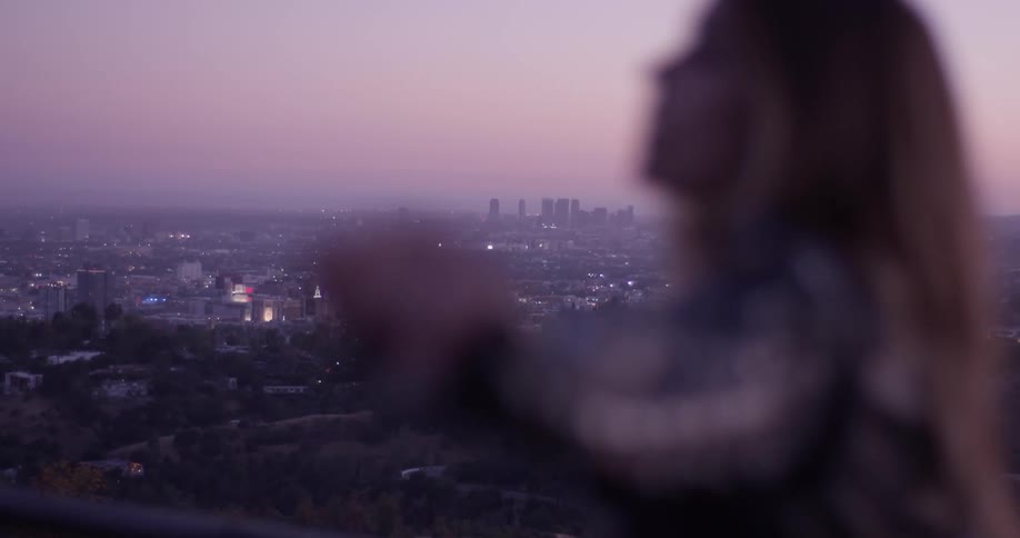 A woman standing at the top of a hill looking at a city