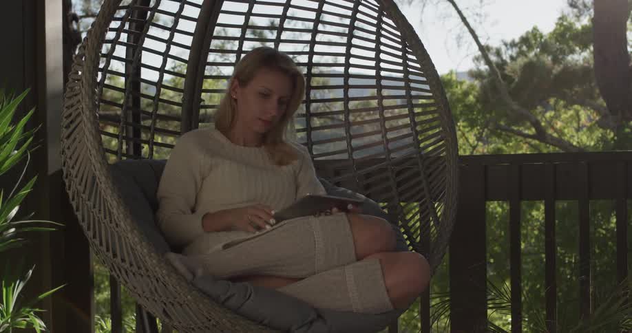 Woman sitting in a circular swing types on a tablet