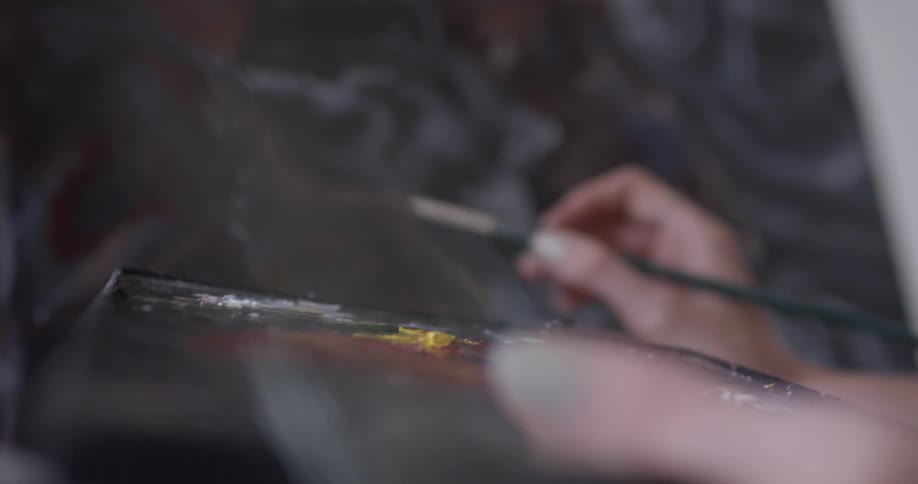 Person holds a pallet of paints and paints on a canvas