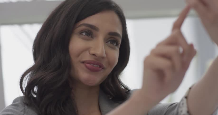 A woman smiles as she takes selfies in a bright room