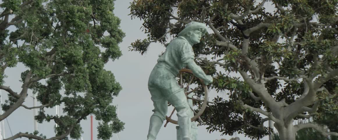 A green statue of a man holding a wheel