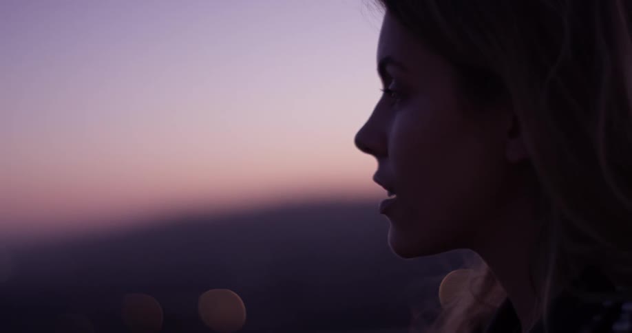A woman stands outside as the sun sets looking at a huge city