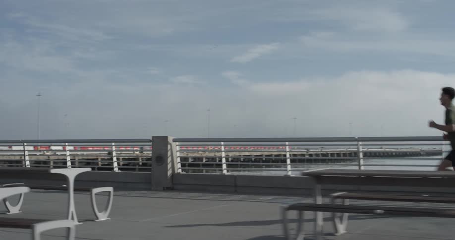 Man running on a sidewalk near a bridge