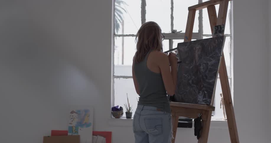 Woman in an art studio painting on a black canvas