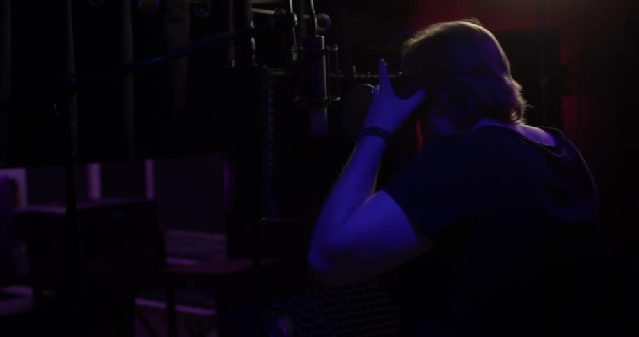 A man puts on headphones and stands at a microphone in a darkened room