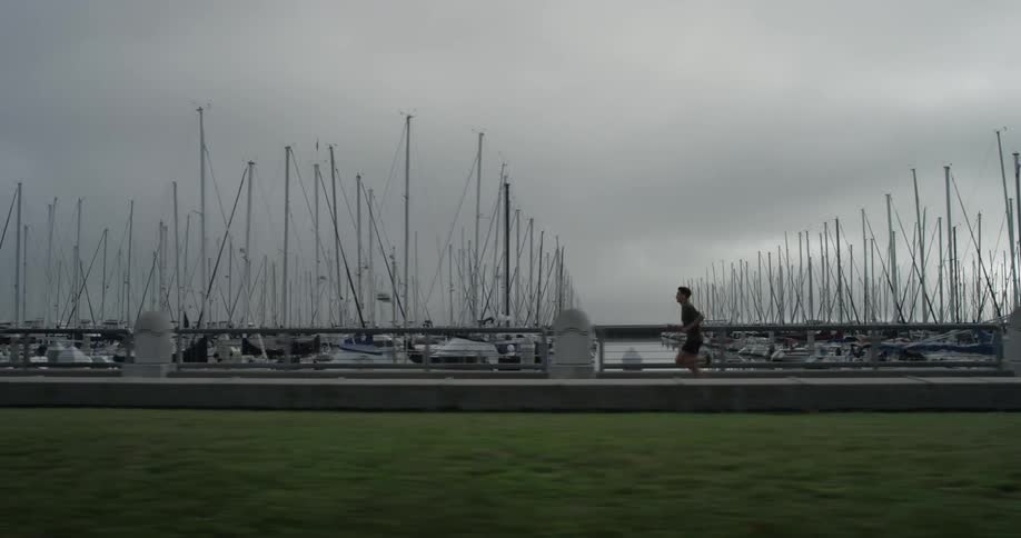 A man running on a path next to a marina on an overcast day