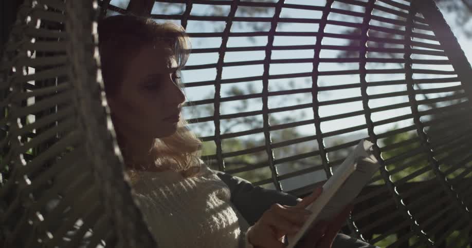A woman sitting in a swing is reading a book