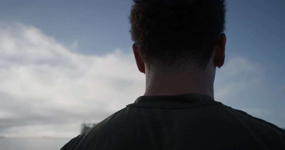 Man looks out over water with earbuds on