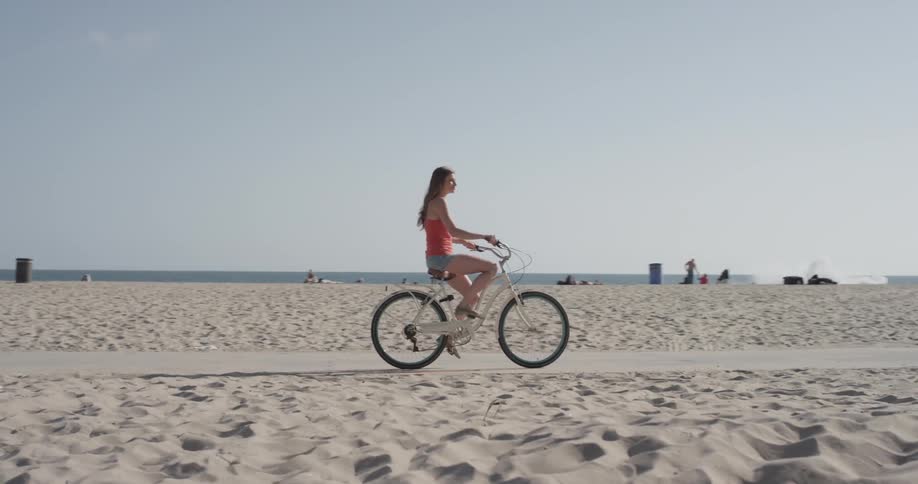 A woman rides her bike along a path cutting through the sand of a beach