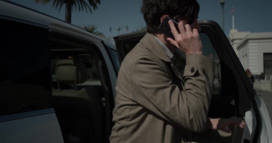 A man getting out of a car while talking on a phone
