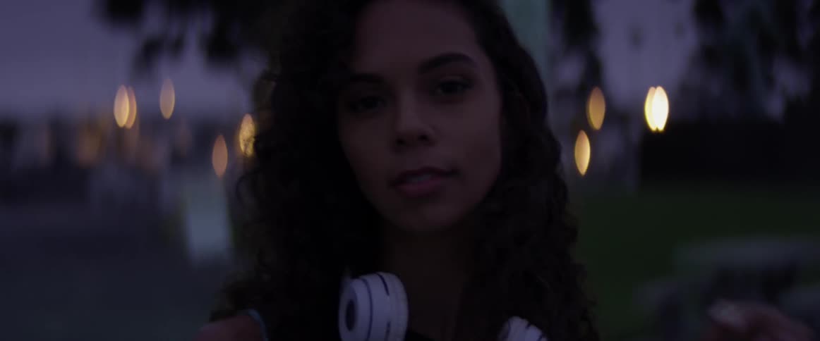 A woman stands in the darkness with headphones around her neck