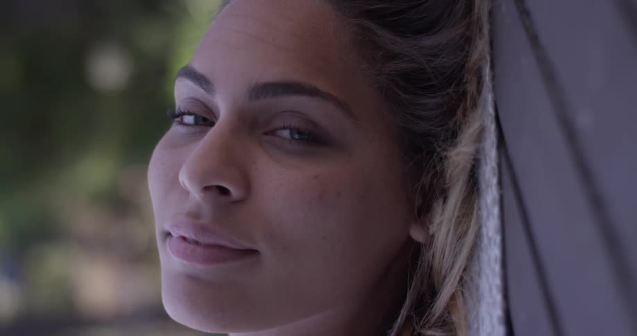 A woman opens her eyes and looks at the camera as she is laying down outside in the sunlight of a nice sunny day