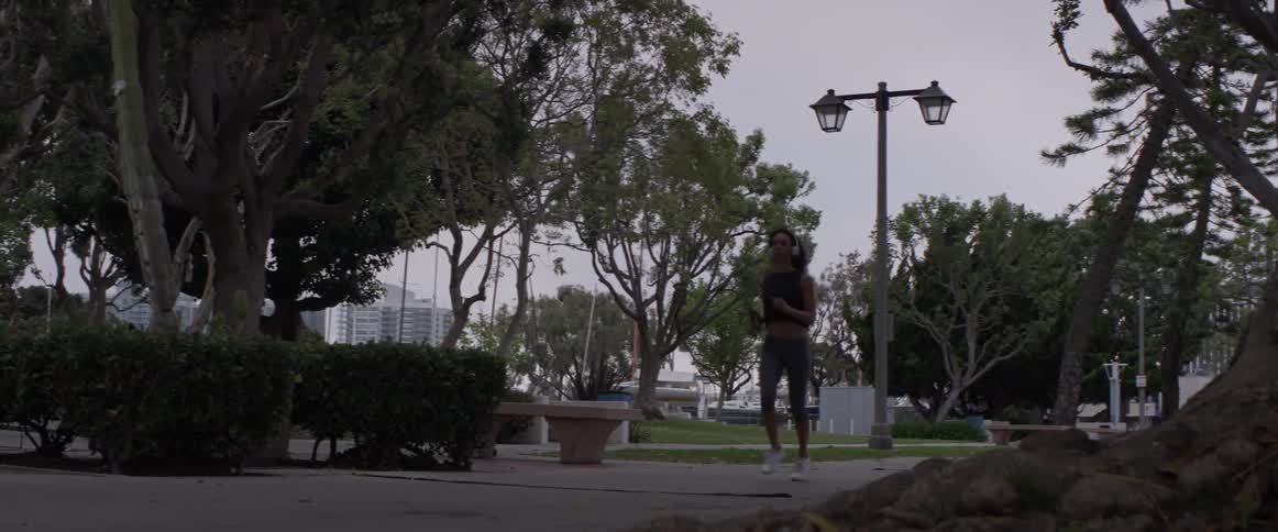 A woman jogging down a sidewalk with headphones on
