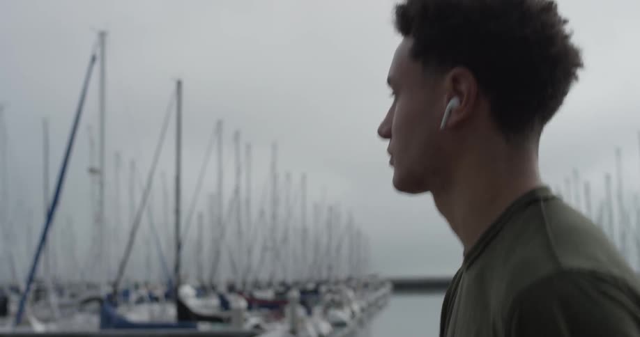 A man walks with ear buds in his ears by a marina