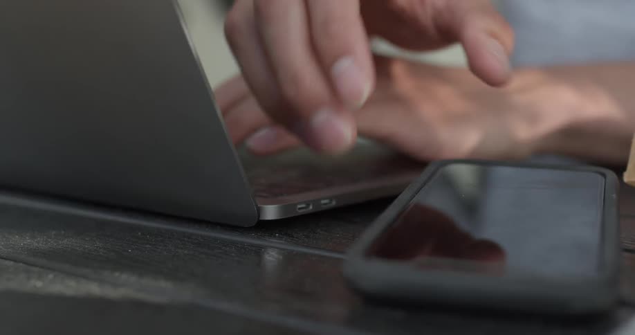Person sits at a desk typing on a laptop and picks up their phone