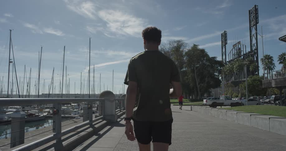 Man walks on the sidewalk by a harbor on a sunny day