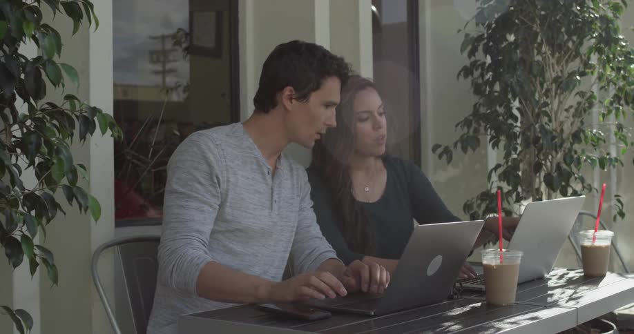 A couple sits on a balcony each with their own laptop