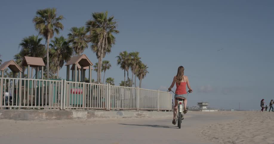 Woman pedals a bike past a playground