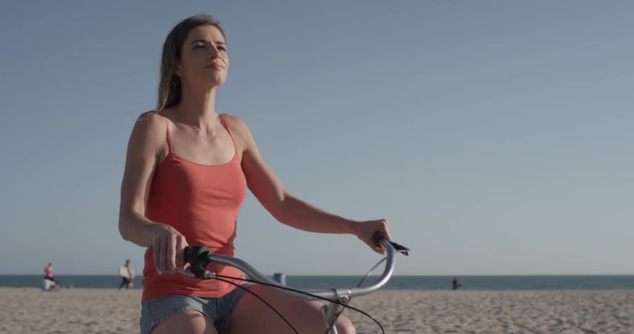 A woman in a tank top riding a bike down the sidewalk at the beach