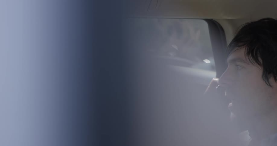A man sits in the backseat of a car talking on the phone