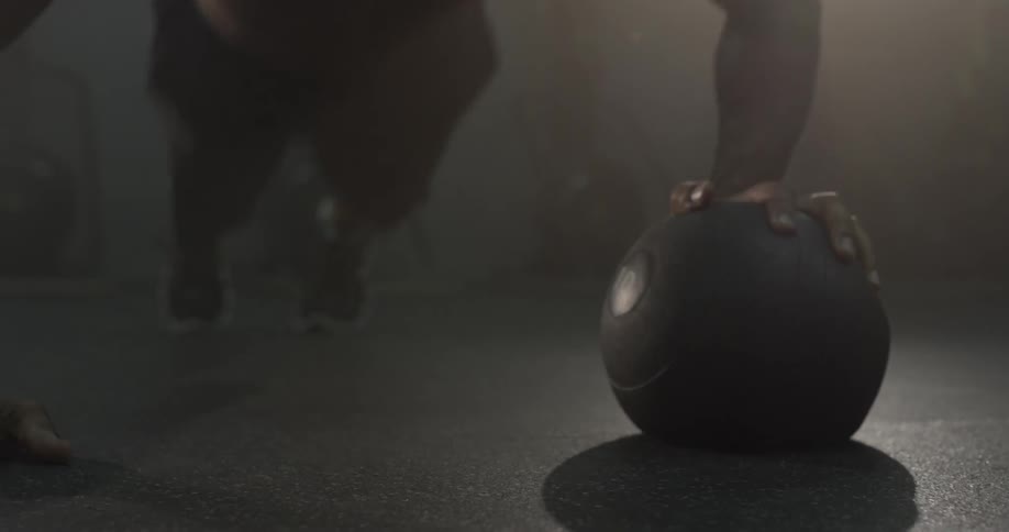 A man with no shirt on doing pushups with a ball