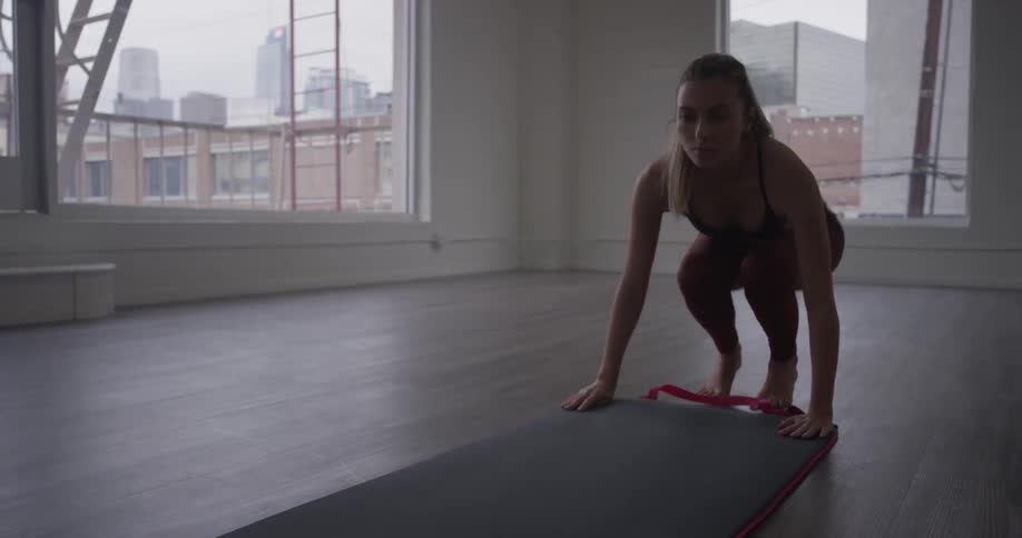 Woman unrolls yoga mat in empty room