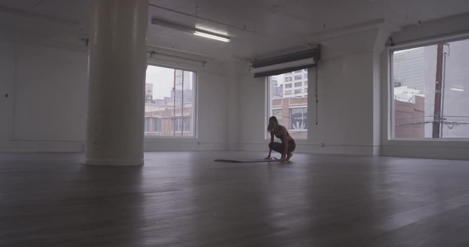 A woman unrolls a yoga mat onto the floor