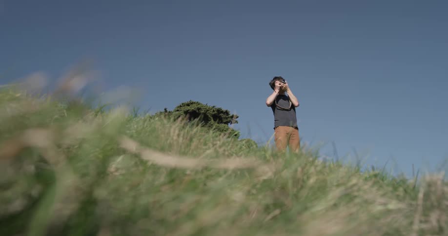 A man stands up on the side of a hill and takes a photograph