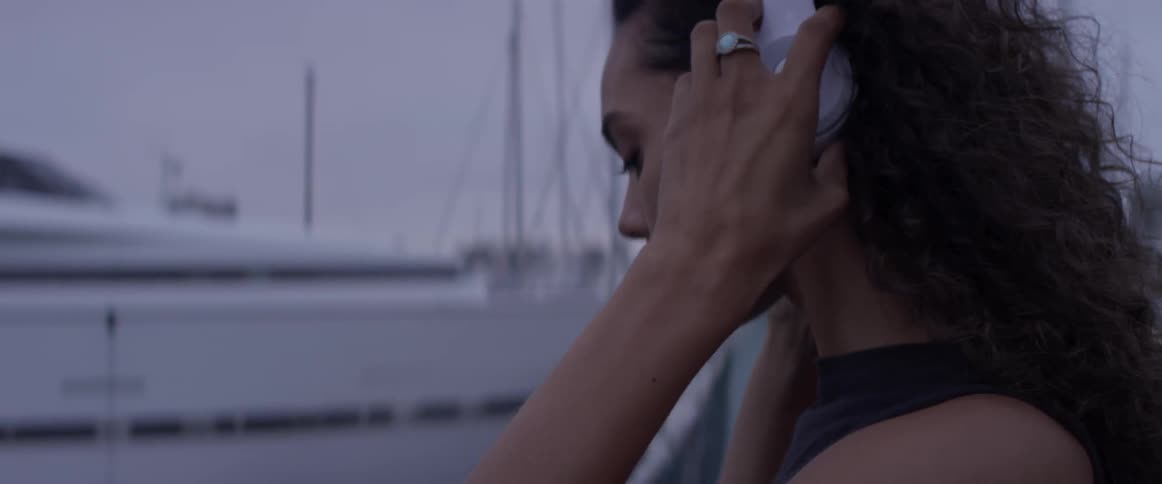 Women is jogging towards the camera and coming into focus then stops and takes off her headphone to look out at the marina on a cloudy day