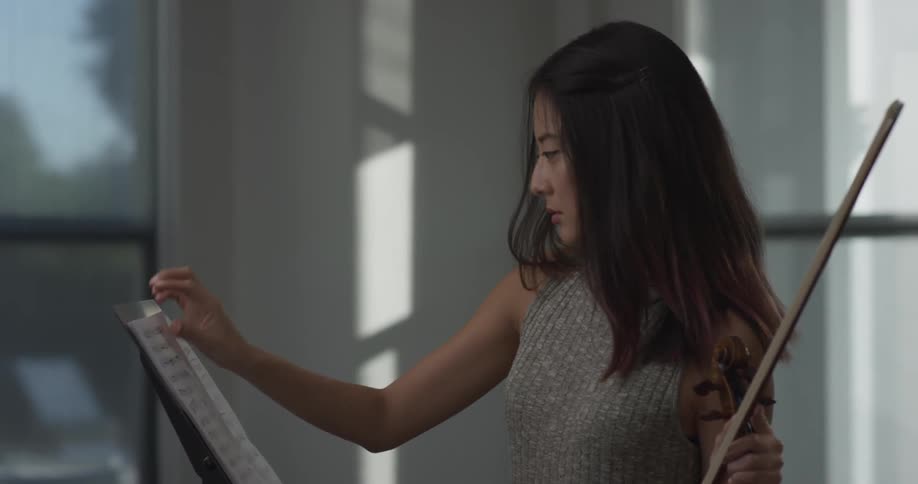 A woman is looking at sheets of music while holding an instrument