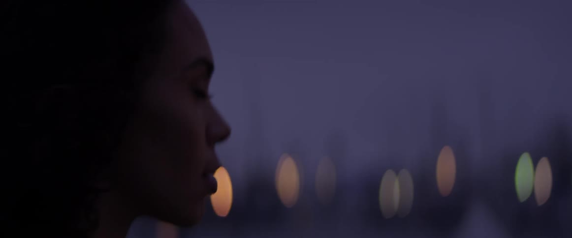 A woman stands in the dark and brushes her hair back