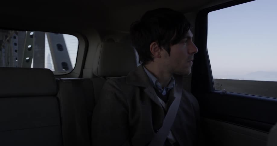 A man sitting in the back of a car driving over a bridge