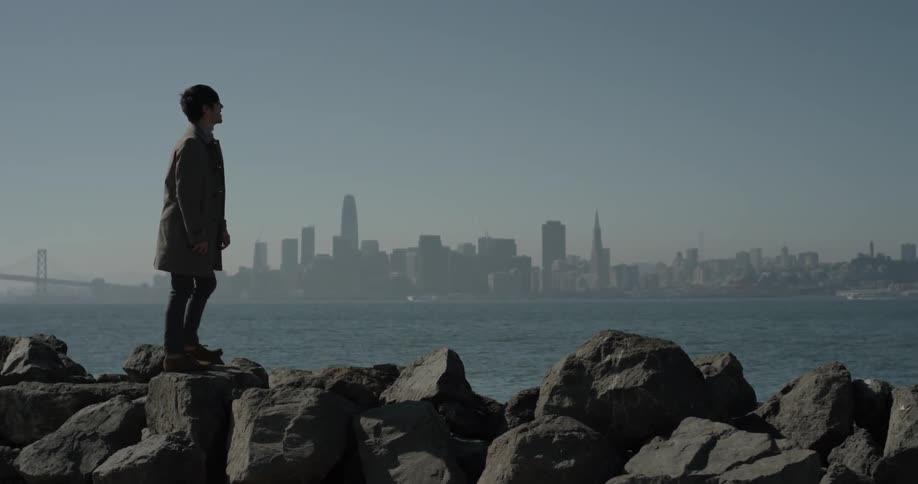 Man walks up onto large rocks looking out at the bay and city