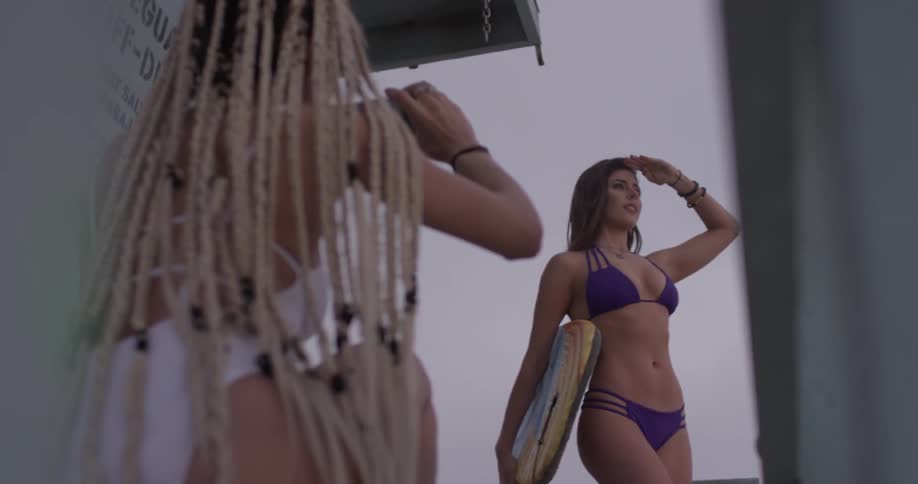 A woman in a bathing suit photographing another woman in a bikini holding a boogie board
