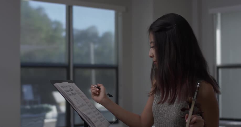 Woman reads sheet music on a stand and writes on it