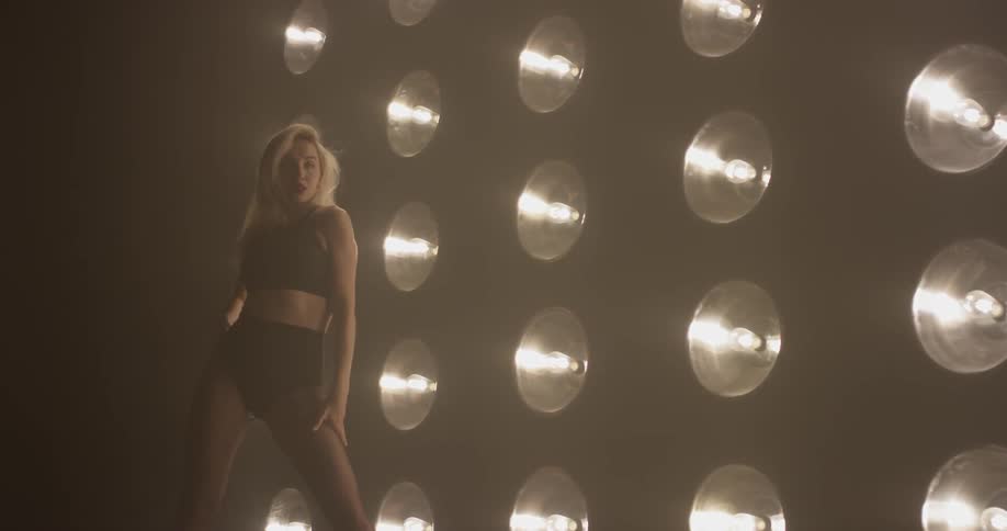 A woman is dancing in front of lights in a dark room