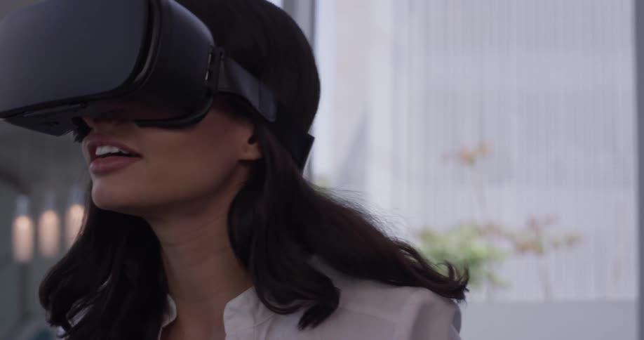 A woman looks around with virtual reality goggles on and appears to be enjoying playing a game