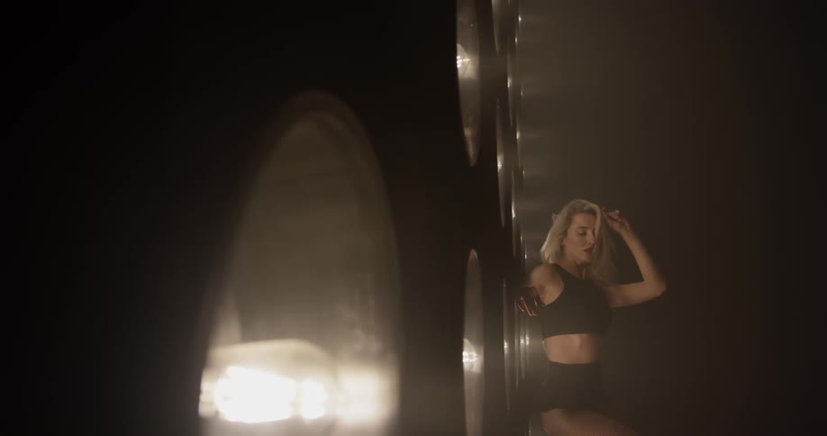 A woman is dancing in front of a bunch of lights cut out and placed in the wall in sexy underwear blond hair and tights