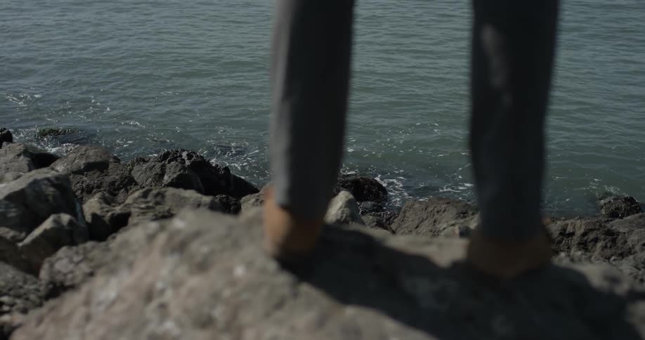 Lower legs stand on a large rock near the ocean