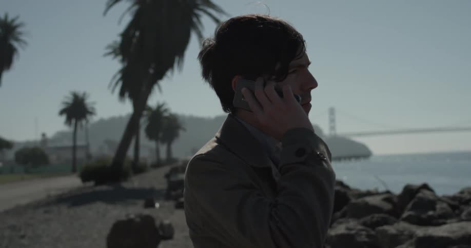 Man near rocks and water talks on cell phone